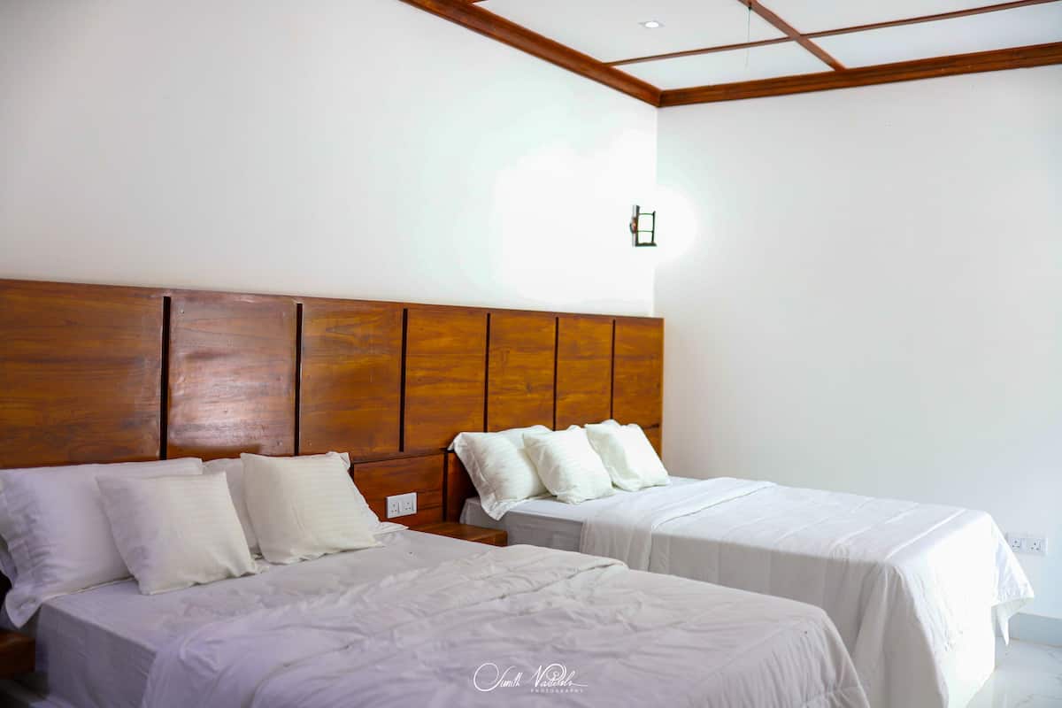 A hotel room with two beds, wooden headboard, white bedding, and a small wall-mounted light fixture.