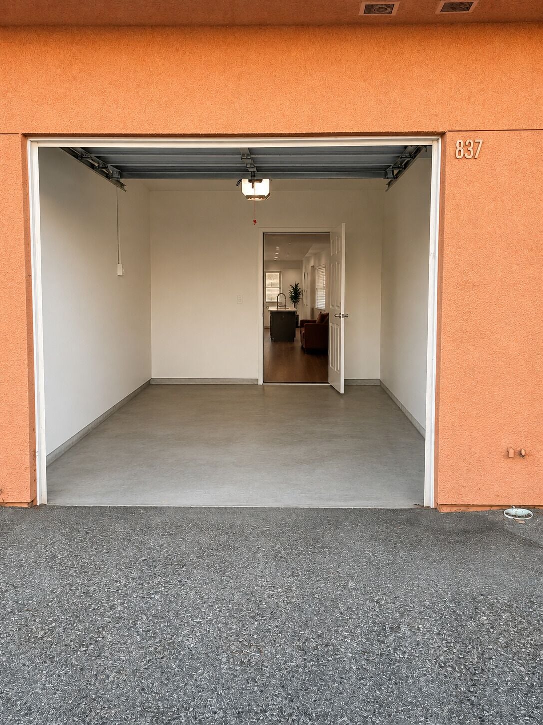 Un garaje con puerta cerrada, el número '837' en la pared y un pasillo que conduce a una sala de estar.