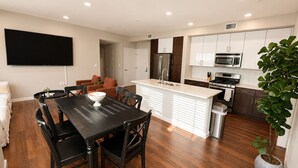 A modern kitchen with white cabinets, a central island, stainless steel appliances, and a dining area with a black table and chairs. - Spacious 3 Bedroom, Close Venice Beach (Marina del Rey)