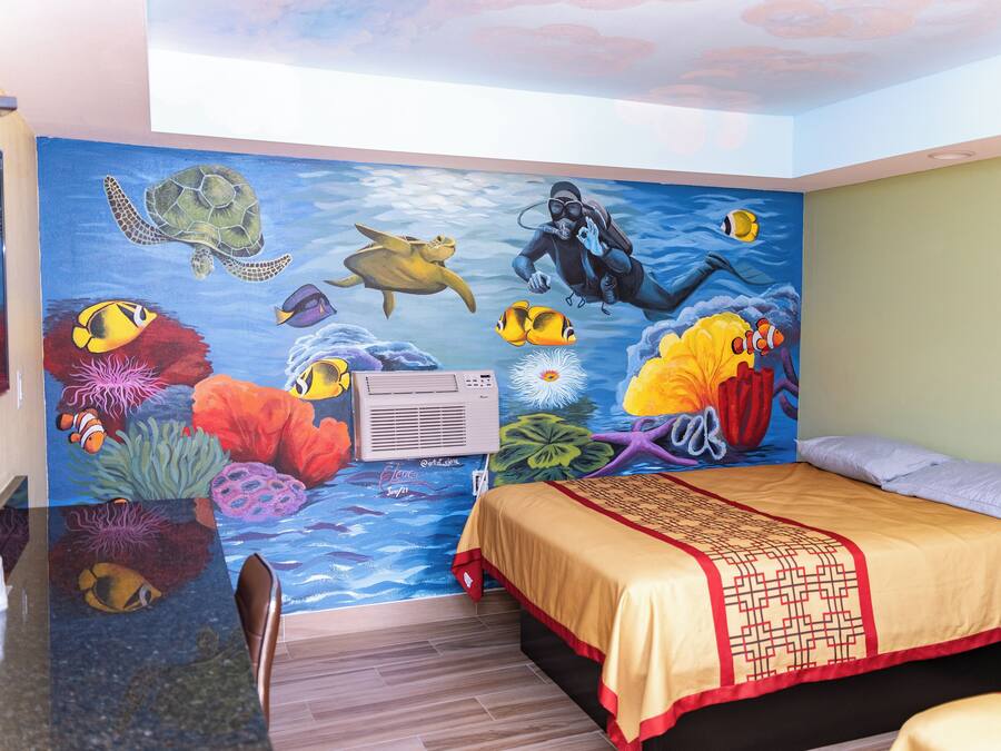 Ein Zimmer mit Wandgemälde von Meereslebewesen, einem Bett mit gemustertem Überwurf und einem Schreibtisch mit Stuhl.