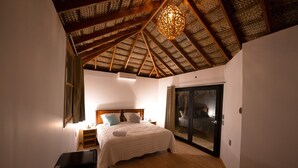 A bedroom with a wooden ceiling, a bed with a white bedspread, a nightstand, and a sliding glass door leading to a balcony. - Panorama Garden Inn (Máncora)