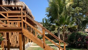 A wooden staircase leading to a thatched-roof structure, surrounded by a well-maintained garden with palm trees and flowering plants. - Panorama Garden Inn (Máncora)