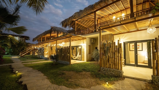 A resort with thatched-roof structures, a stone pathway, and a well-lit entrance. - Panorama Garden Inn (Máncora)