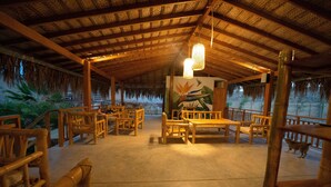 A covered outdoor seating area with wooden furniture and a thatched roof. - Panorama Garden Inn (Máncora)