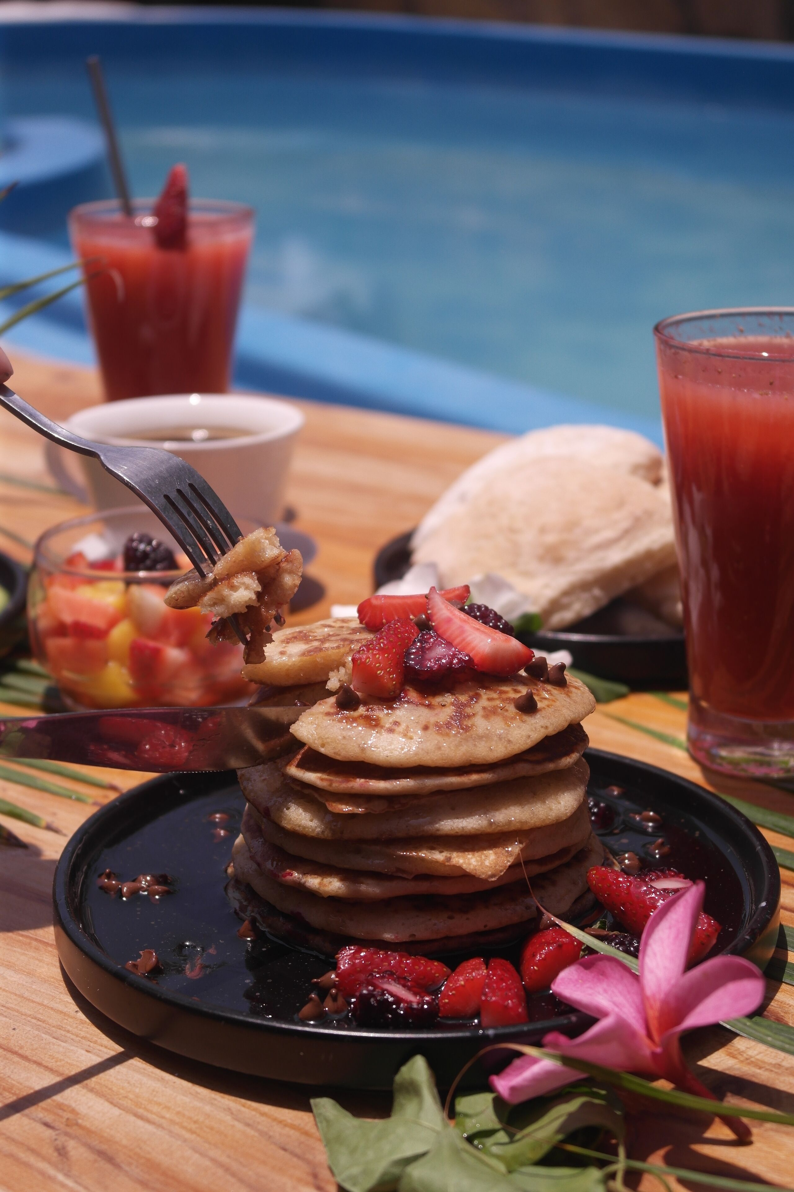 Una pila de panqueques con fresas y una bebida junto a una piscina.