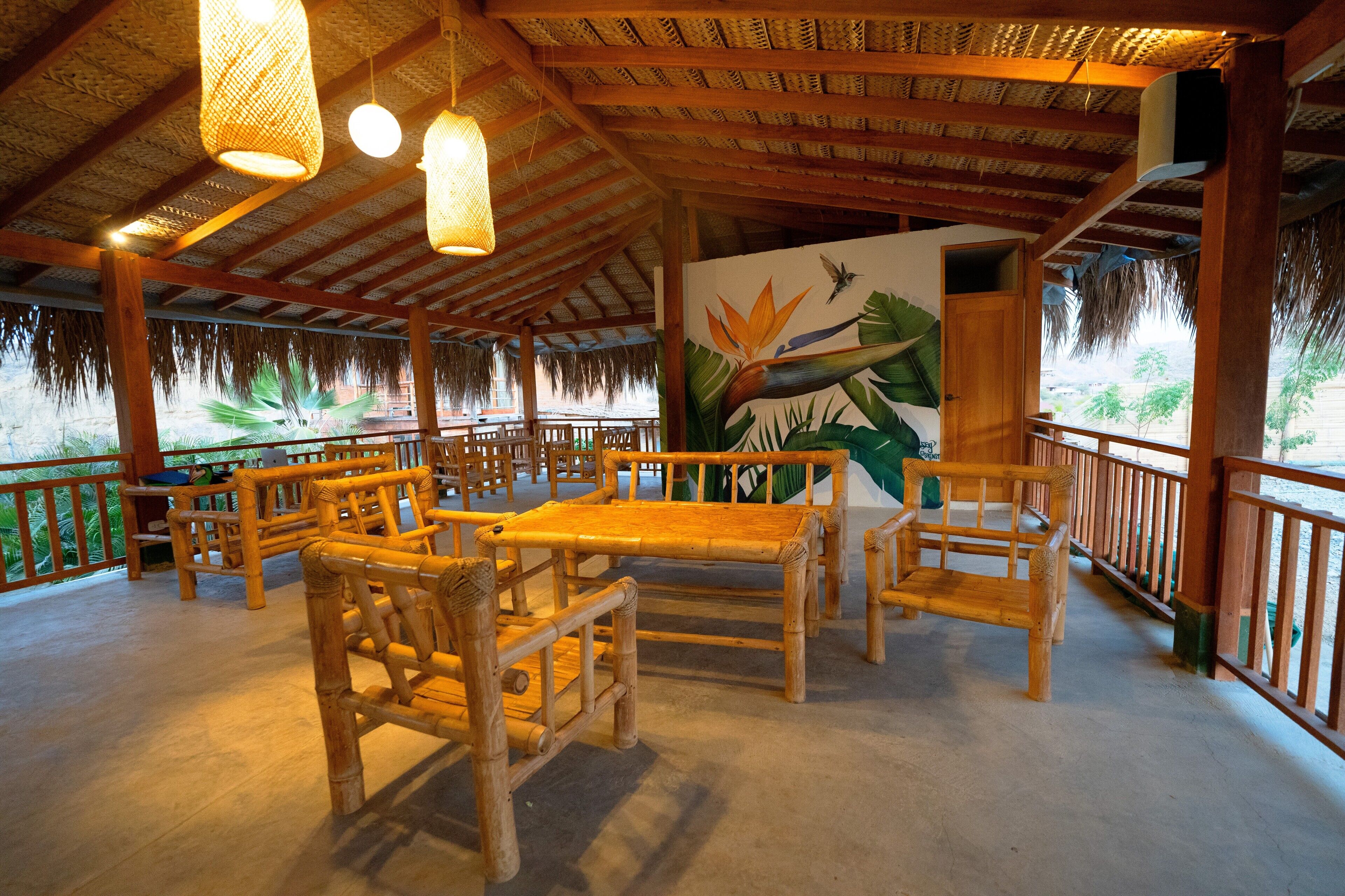 Un área de estar al aire libre cubierta con mobiliario de madera y un mural de un pájaro y plantas.