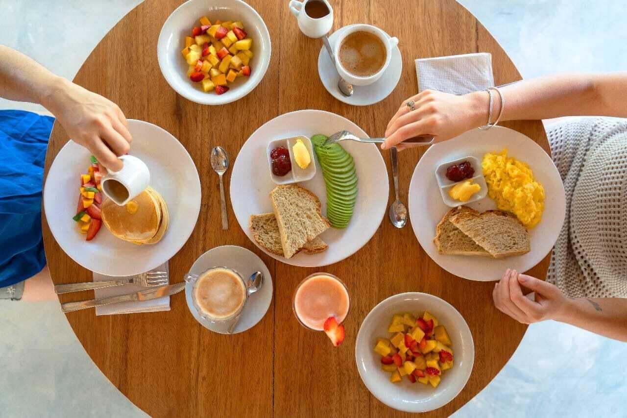 Ett runt träbord med frukosttallrikar som innehåller rostat bröd, frukt och drycker.