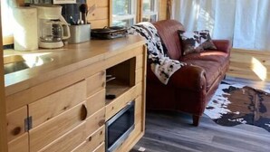 Un interior de cabaña acogedor, con una kitchenette de madera, un sofá de cuero rojo y un ventanal grande.