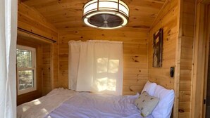 Un dormitorio de cabaña de madera con cama, ventilador de techo y ventana con cortinas.