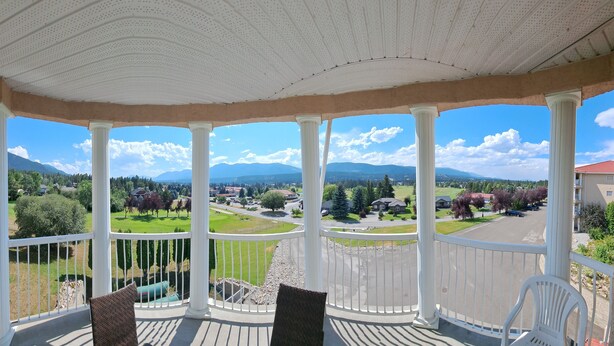 A covered balcony with white columns, offering a view of a residential area with houses, trees, and mountains in the background. - Spacious pet friendly condo with beautiful golf course and mountain views (Fairmont Hot Springs)