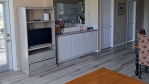 A modern living room with a wooden coffee table, a television on a cabinet, and a kitchen in the background. - Spacious pet friendly condo with beautiful golf course and mountain views (Fairmont Hot Springs)