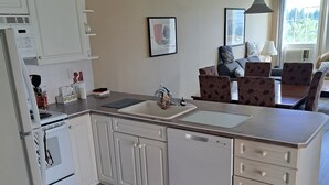 A kitchen with white cabinets, a dishwasher, a stove, and a sink. There is a dining area with a table and chairs. - Spacious pet friendly condo with beautiful golf course and mountain views (Fairmont Hot Springs)