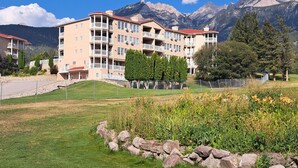 A multi-story hotel with balconies, set against a backdrop of mountains and clear blue sky. - Spacious pet friendly condo with beautiful golf course and mountain views (Fairmont Hot Springs)