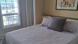 A neatly made bed with a quilted bedspread, a pillow with a floral pattern, and a framed landscape painting on the wall. - Spacious pet friendly condo with beautiful golf course and mountain views (Fairmont Hot Springs)