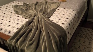 Een bed met beddengoed met een patroon, een groene deken en decoratieve kussens.