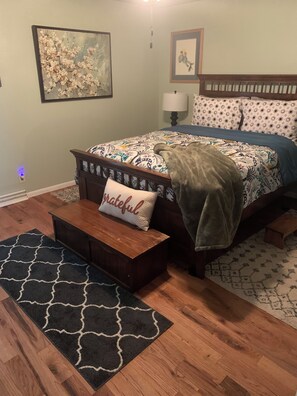 Un dormitorio con una cama, una mesita de noche, una silla, una alfombra y un cuadro en la pared.