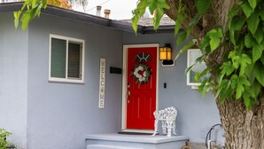 Una casa con puerta roja, un cartel de bienvenida, un adorno floral y una silla blanca en el exterior.