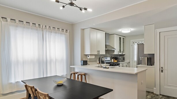 A modern kitchen with white cabinets, a black countertop, and a dining area with a black table and wooden chairs. - 3 BLK Walk to Funky DT Ferndale's Restaurants & Bars/20 Min Drive to DT Detroit (Ferndale)