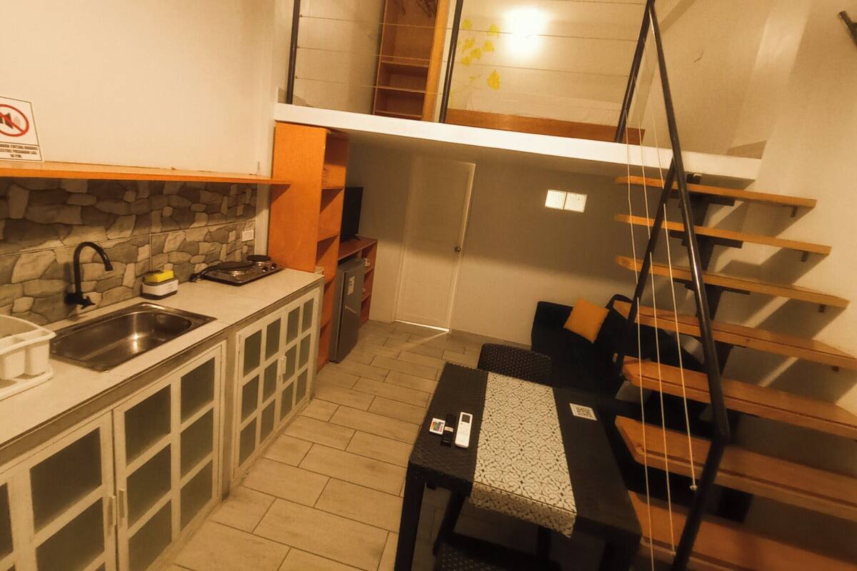 A compact kitchen with a stone backsplash, a built-in stove, and a sink. There is a small dining area with a table and chairs.