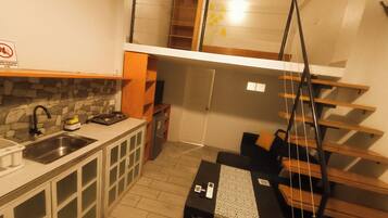 A compact kitchen with a stone backsplash, a built-in stove, and a sink. There is a small dining area with a table and chairs.