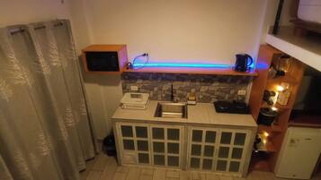 A compact kitchen with a built-in refrigerator, a sink, and a countertop with a kettle.