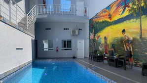 A swimming pool with tiled flooring, a staircase with white railings, and a mural on the wall depicting a tropical scene. - La Quinta Loft Apartments (Iquitos)