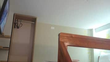 A bedroom with a wooden bed frame, a TV mounted on the wall, a wooden wardrobe, and a small bedside table.
