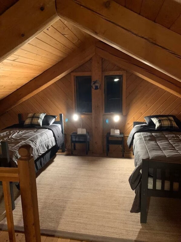 A cozy attic bedroom with two beds, a wooden ceiling, and a small window.