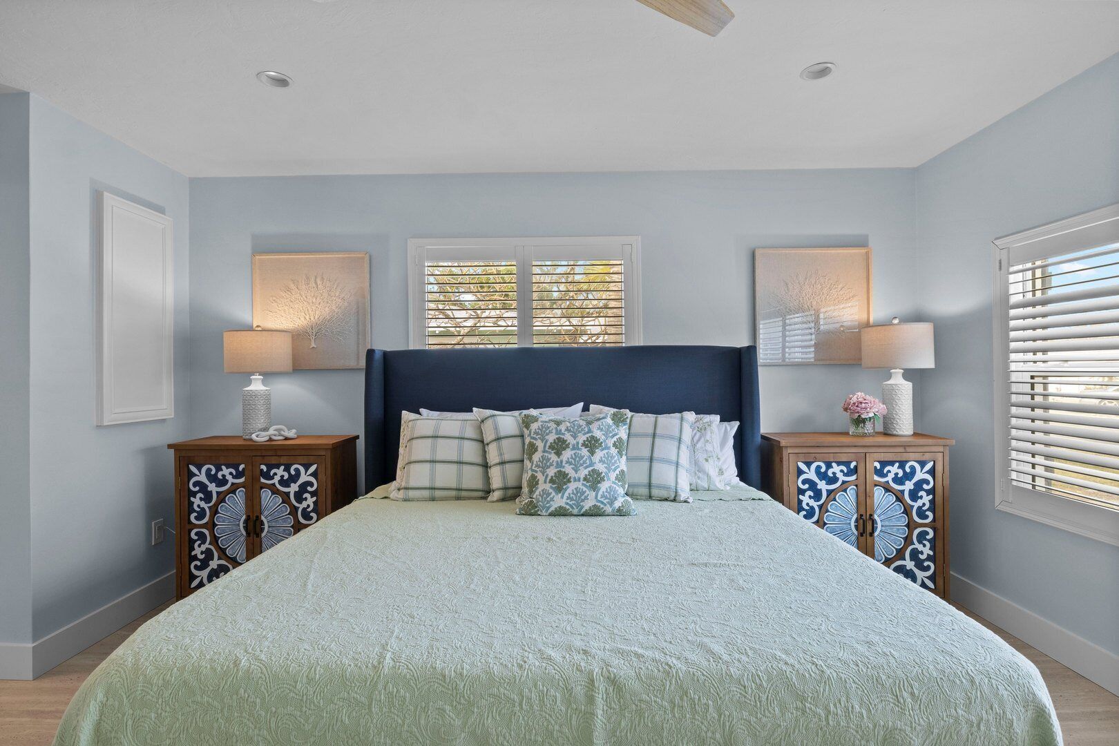 A bedroom with a large bed, two nightstands, a ceiling fan, and a window with blinds.