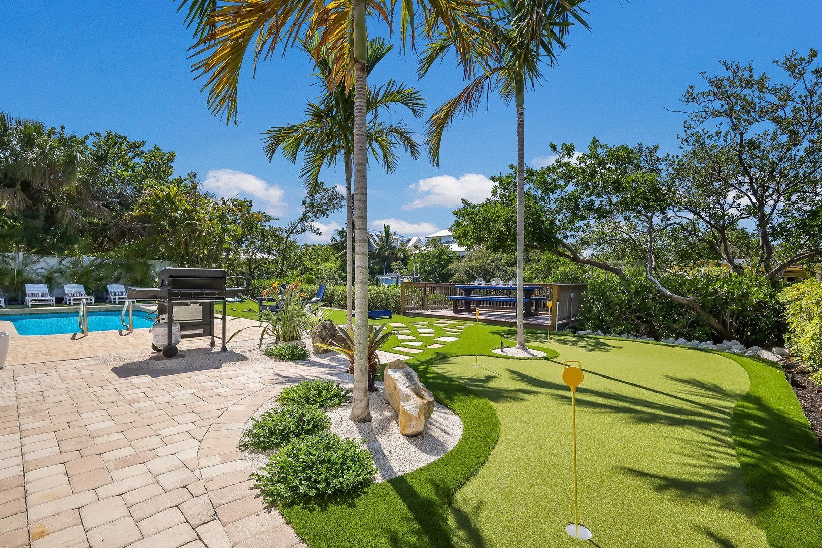 Un espace piscine comprenant un green d’entraînement au golf, des chaises longues et un barbecue.