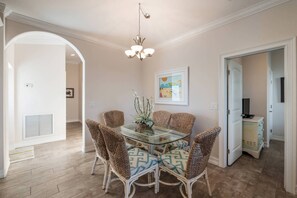 A dining area with a glass table surrounded by wicker chairs, a chandelier, and a framed artwork on the wall. - Surfs Up: 2 Blocks to Beach! Private Pool & Spa! by Anna Maria Life Vacation Rentals (Holmes Beach)