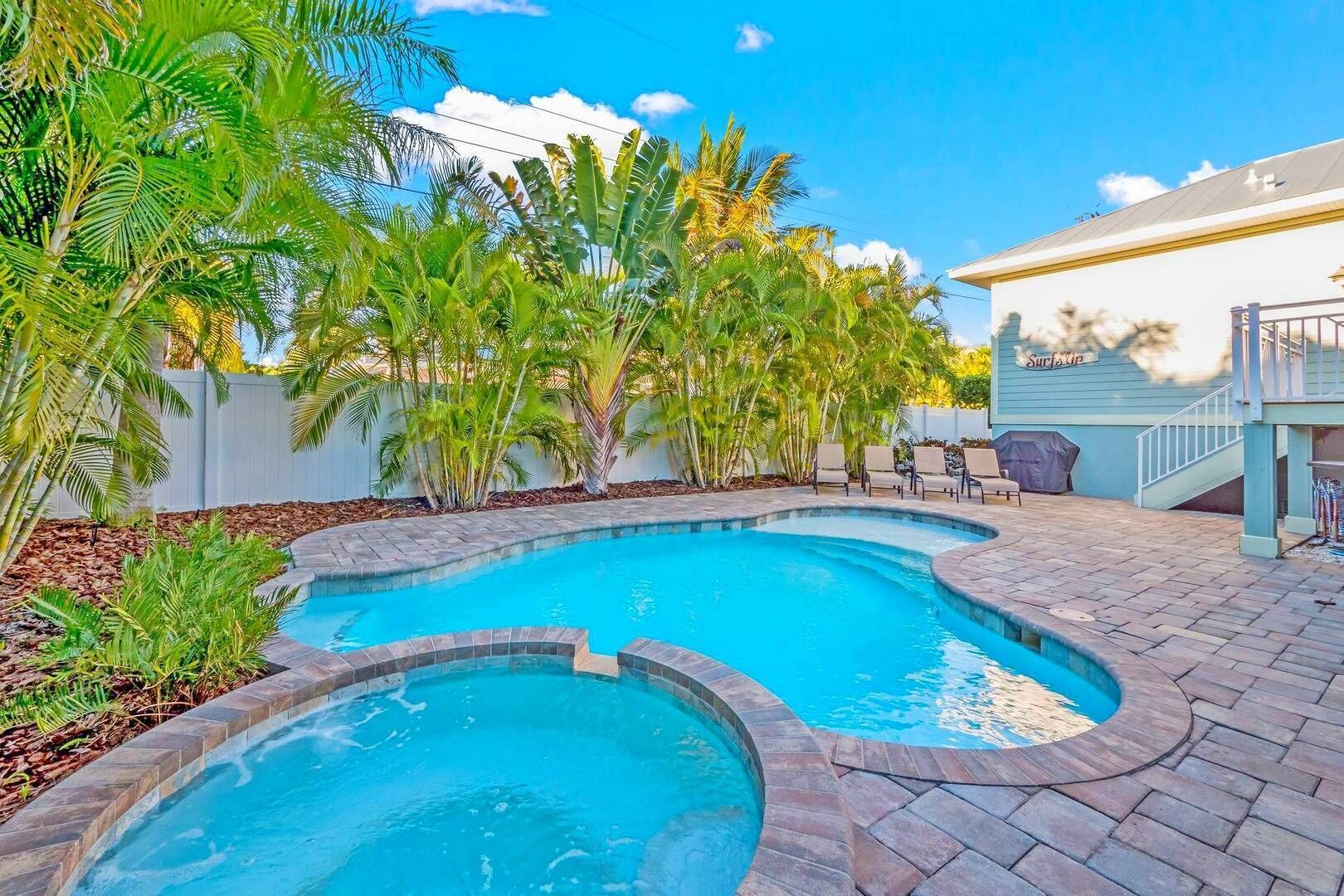 A swimming pool with a curved design, surrounded by a brick patio and palm trees.