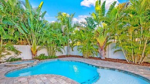 Une piscine au design incurvé, entourée d’une terrasse en briques et de plantes tropicales luxuriantes.