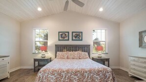 Une chambre à coucher comprenant un lit, deux tables de chevet, deux lampes fixées au mur, un ventilateur de plafond et deux œuvres d’art encadrées.