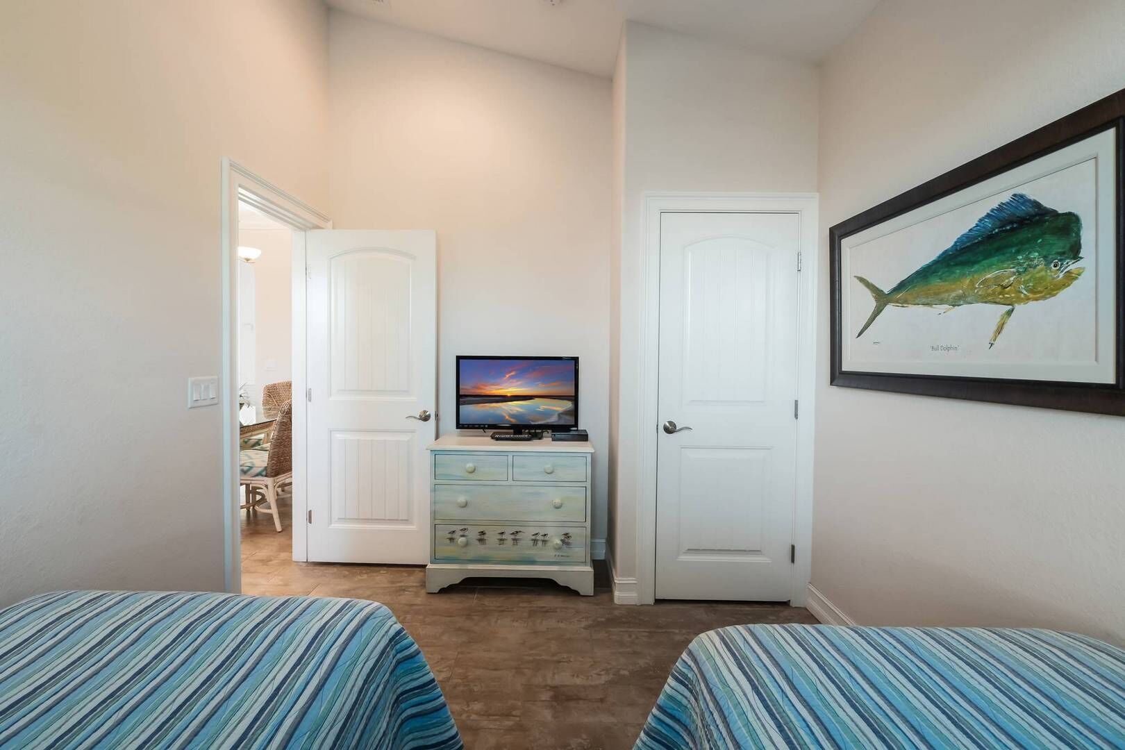 A bedroom with two beds, a television on a dresser, and a framed fish painting on the wall.