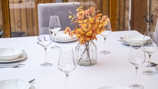 Una mesa servida con platos blancos, copas de vino y un florero con flores amarillas.