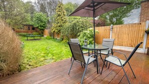 Una terraza de madera con una mesa redonda y sillas, una mesa de picnic y una valla de madera.