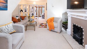 Una sala de estar con sofá, sillón, mesa de centro, chimenea y estantería.