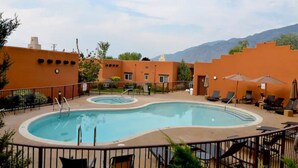 A swimming pool with lounge chairs and umbrellas, surrounded by orange buildings with a mountainous backdrop. - Osoyoos Lakeside 2 BDRM Condo! (Osoyoos)