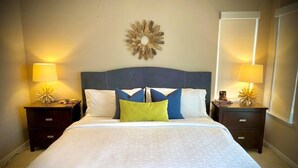 A neatly made bed with a blue headboard, two bedside tables with lamps, and a decorative wall piece. - Osoyoos Lakeside 2 BDRM Condo! (Osoyoos)