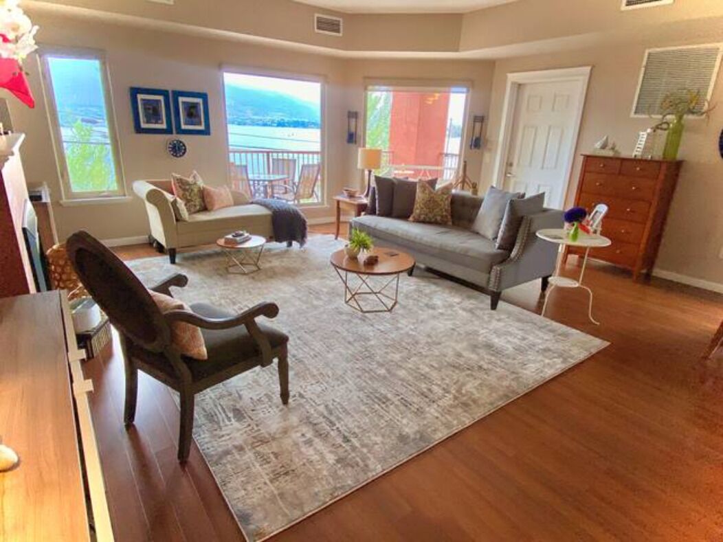 A spacious living room with a large window, a sofa, a coffee table, and a wooden dining table.