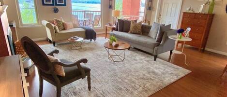 A spacious living room with a large window, a sofa, a coffee table, and a wooden dining table.