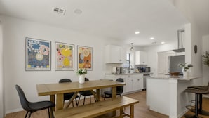 Una cocina moderna con armarios blancos, una mesa de comedor de madera y una pequeña isla con taburetes de bar.