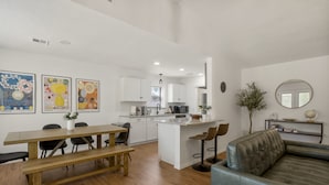 Una cocina moderna con armarios blancos, una isla central y un comedor con mesa de madera y bancos.
