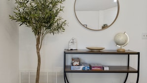 Una habitación con una planta en maceta, un espejo redondo, un globo terráqueo y una estantería con libros y un cuenco.