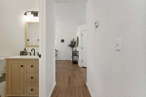 Ein Korridor mit Holzboden, weißen Wänden, einem Holzkabinett mit Schubladen, einem Spiegel und einem kleinen Tisch mit einer Pflanze.