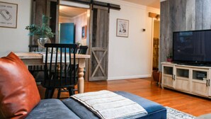 A living room with a sofa, a television, and a dining area with a table and chairs. - Alice Rocks- Pet Friendly, Firepit, WiFi (Frenchburg)