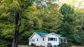A white house with green shutters, surrounded by dense trees and a gravel driveway. - Alice Rocks- Pet Friendly, Firepit, WiFi (Frenchburg)