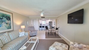 A living room with a sofa, a coffee table, an ottoman, a TV, and a dining area with chairs and a table. - CP 326 Ocean View Condo- Welcome to Paradise (Fort Pierce)