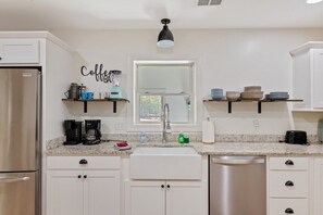 A modern kitchen with white cabinets, a stainless steel refrigerator, a coffee station, and a sink with a faucet.